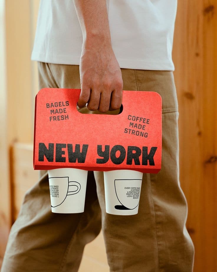 Hand carrying two coffee cups in a bright red cardboard carrier