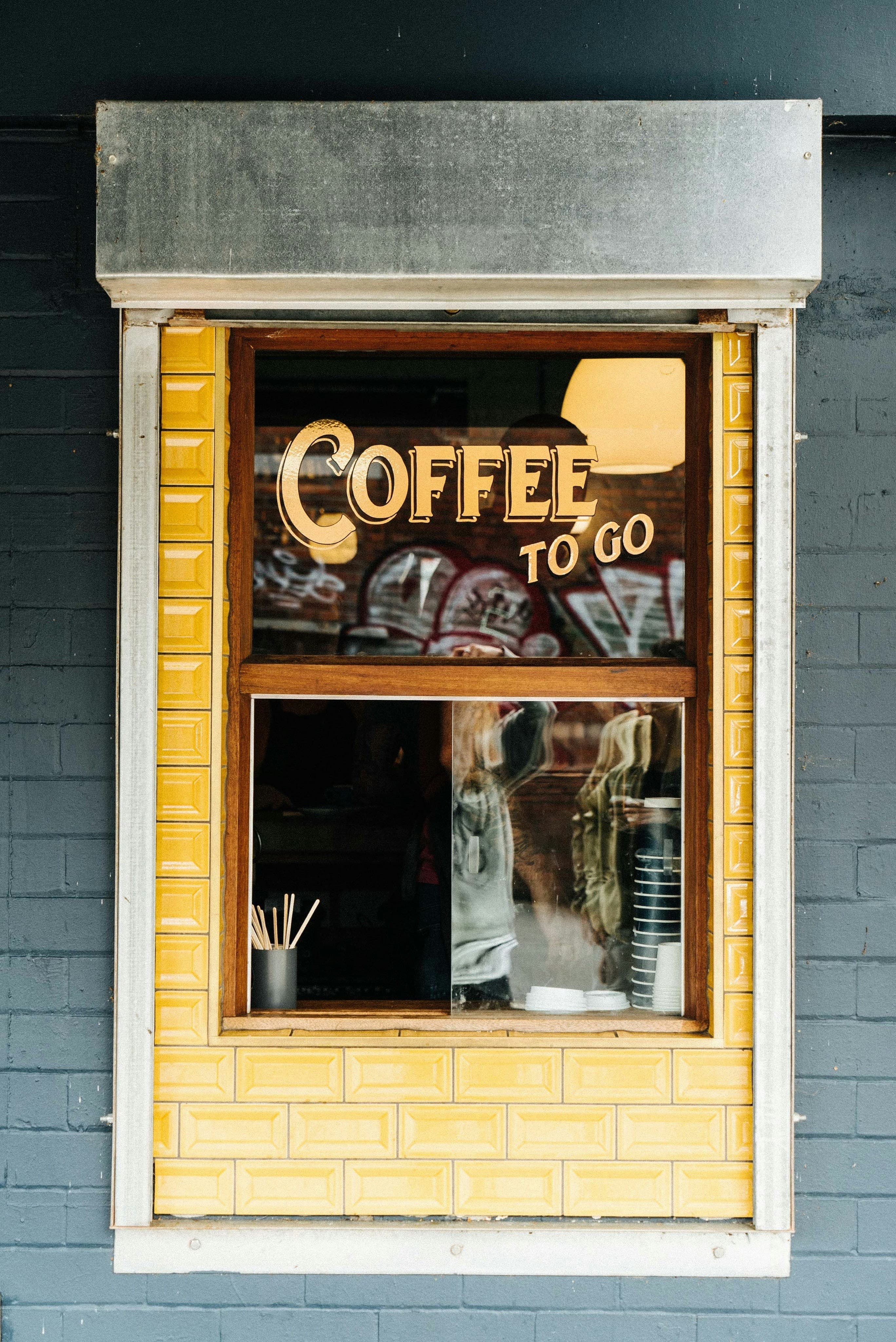 Yellow-tiled coffee-to-go takeout window with hand-painted gold lettering